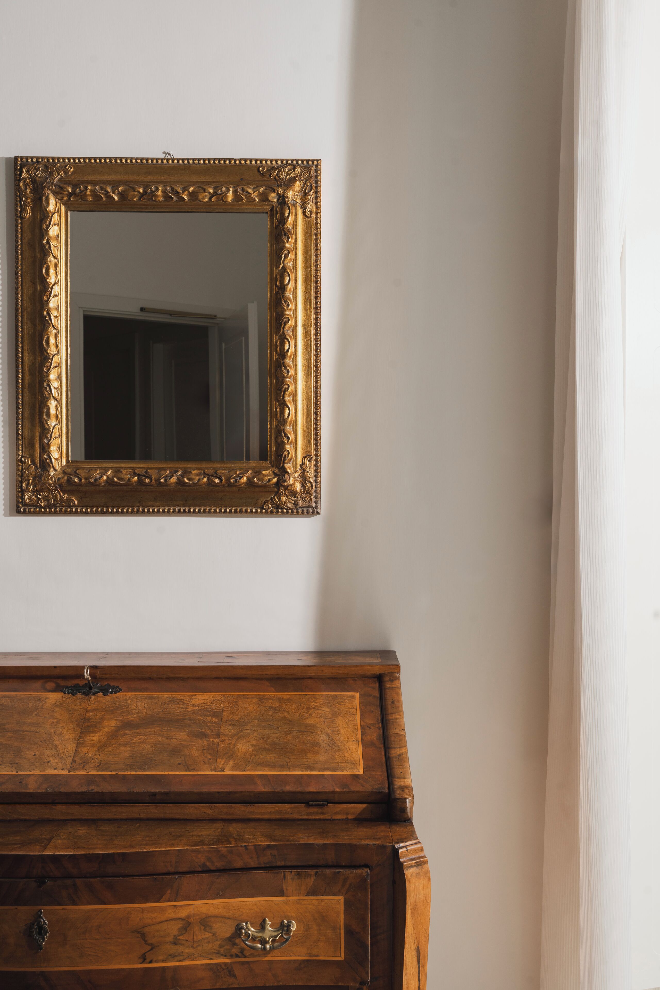 Une commode en bois surmontée d’un miroir à cadre doré.