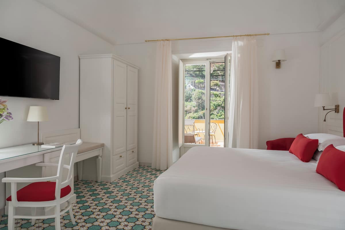 Une chambre d’hôtel équipée d’un lit, d’un bureau, d’une chaise, d’une télévision et d’un balcon donnant sur un paysage verdoyant.