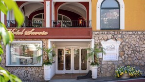 Entrada de hotel con fachada de piedra, un balcón con asientos y un cartel que indica un restaurante.