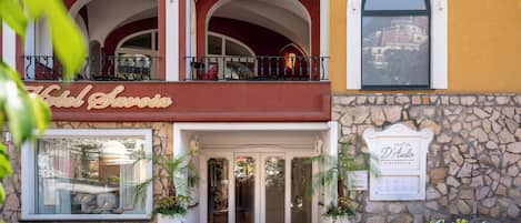 A hotel entrance with a stone facade, a balcony with a railing, and a sign for a restaurant.