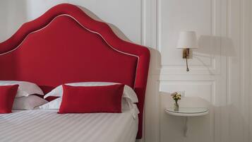 A neatly made bed with red and white bedding, a red upholstered headboard, and a small bedside table with a lamp and a vase of flowers.