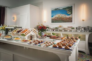 A buffet with a variety of food items, including pastries and fruits, in a well-lit room with a painting on the wall. - Hotel Savoia (Positano)