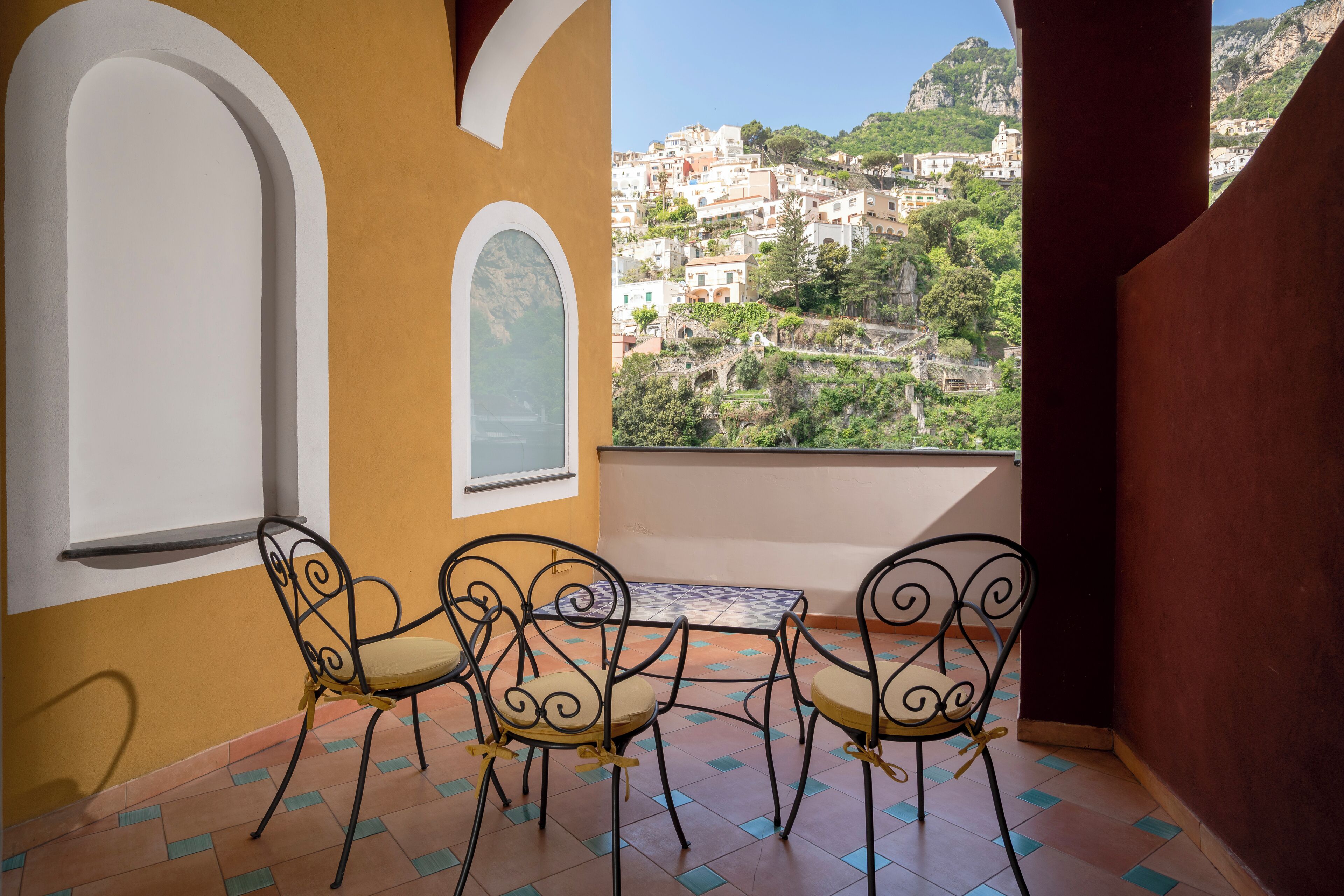Un balcon avec une table et quatre chaises, donnant sur une ville située sur une colline.