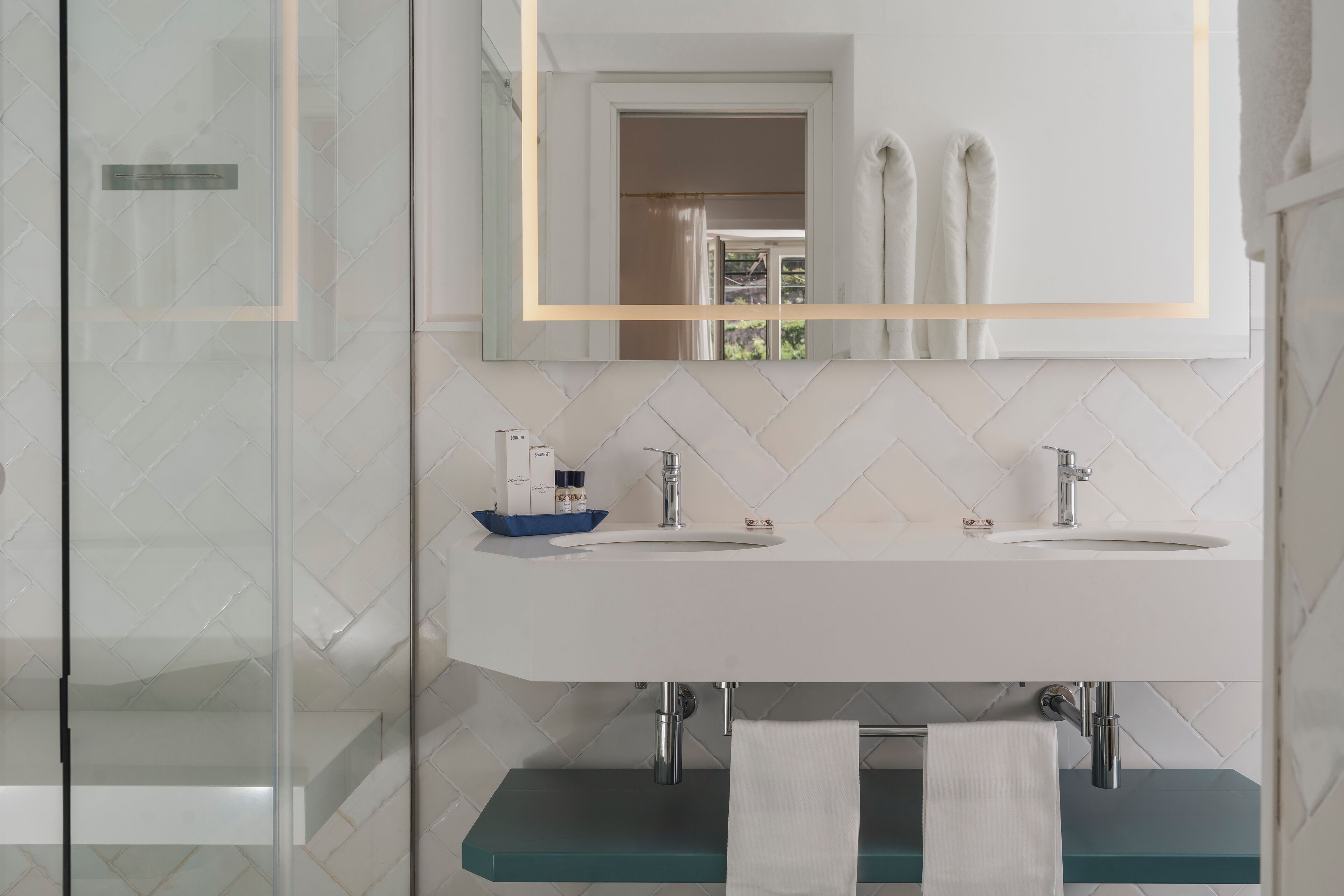 A modern bathroom with two sinks, a glass shower enclosure, and a mirror with a gold frame.