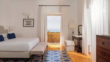 A hotel room with a bed, a small table, a chair, a dresser, and a view of the sea through a window.
