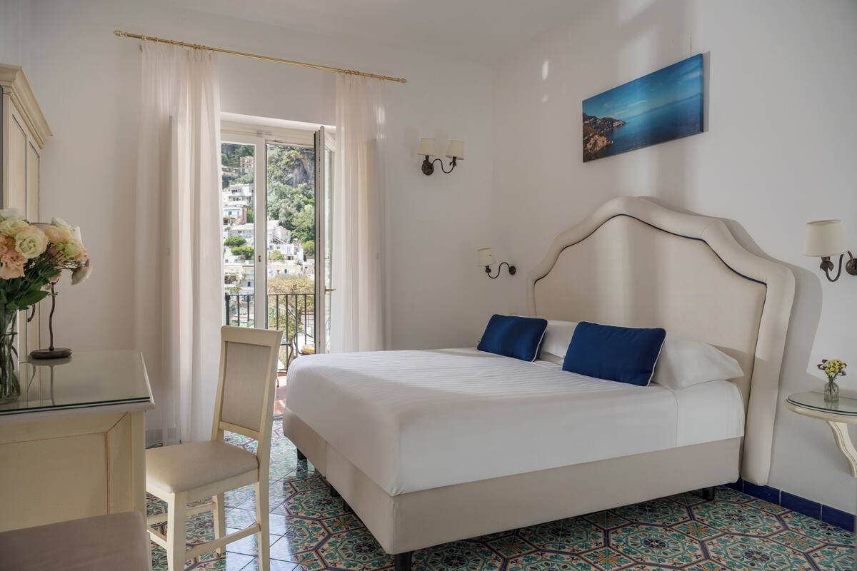 Une chambre à coucher comprenant un lit, une chaise, une petite table, un tableau et une vue sur un balcon.