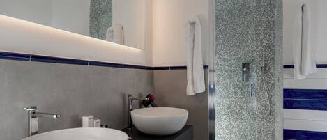 Un baño moderno con dos lavamanos grandes de color blanco, un espejo y una zona de ducha con mosaicos.