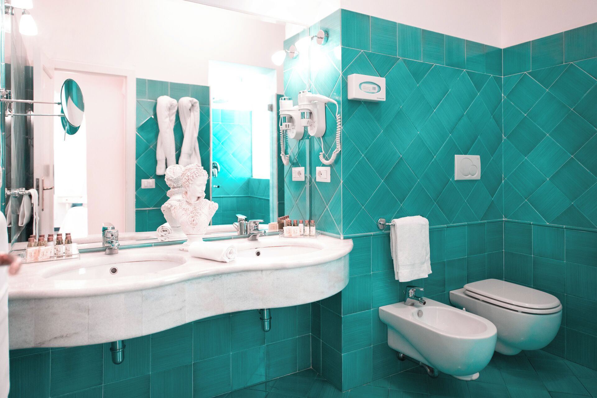 Et badeværelse med et stort spejl, to håndvaske, et bidet og et toilet.