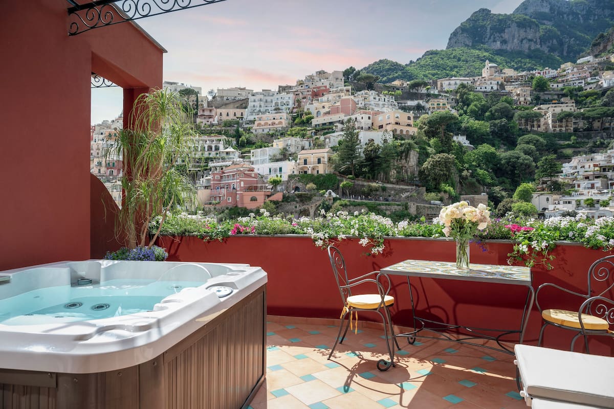 Un balcon avec un jacuzzi, une table et des chaises, donnant sur une ville située sur une colline.