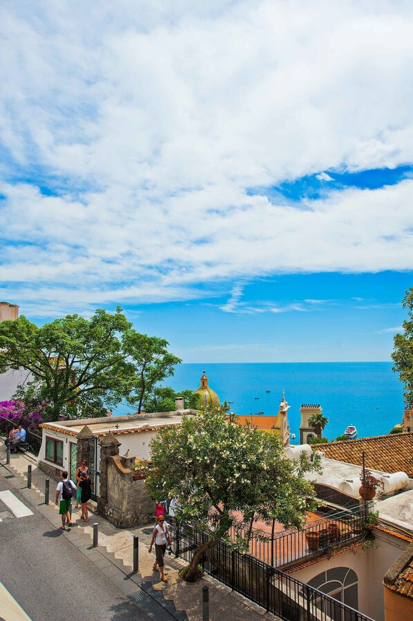 A coastal street with buildings, a tree-lined path, and a view of the sea. - Hotel Savoia (Positano)