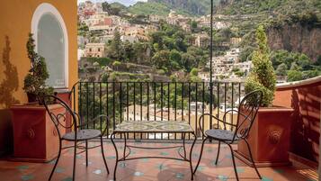 Un balcon avec deux chaises et une table, donnant sur une ville située sur une colline, avec ses bâtiments et sa végétation.
