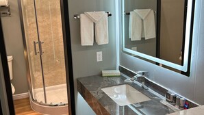 A modern bathroom with a glass shower enclosure, a large mirror, and two sinks. - Mountain View Motel (Bishop)