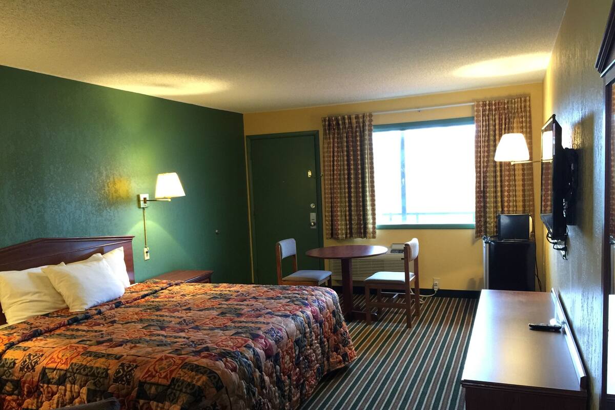 Une chambre d’hôtel avec un lit, un bureau, une chaise, une télévision et une fenêtre avec des rideaux.