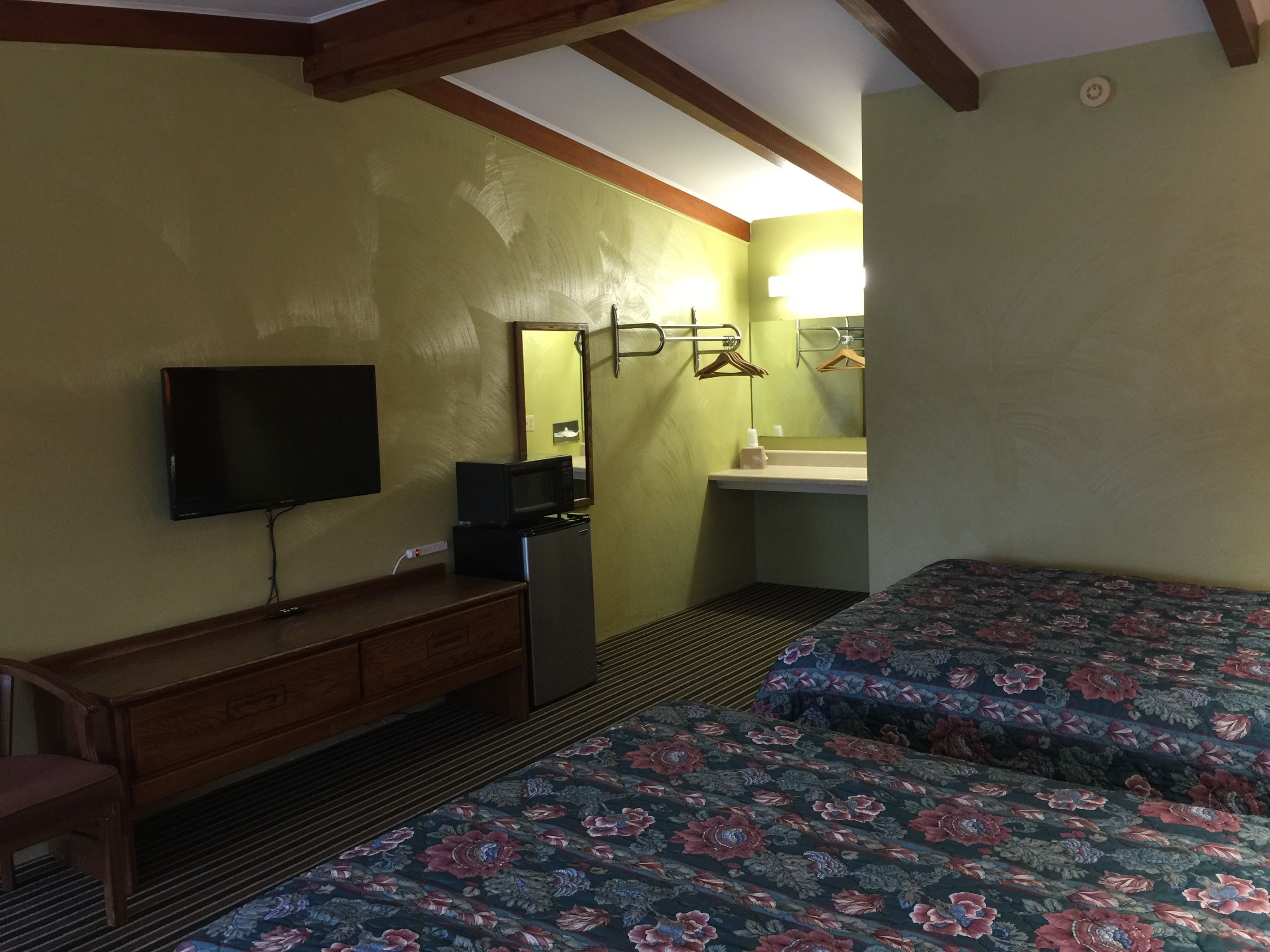 A hotel room with a bed, a TV, a dresser, a microwave, and a bathroom with a mirror and sink.