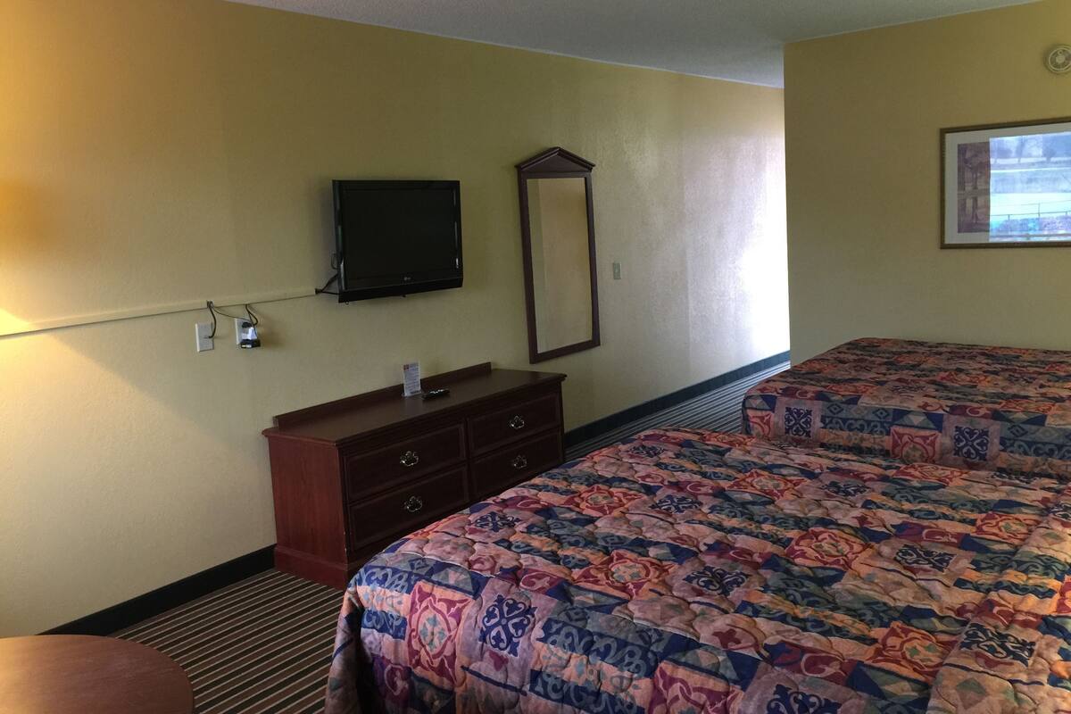 Une chambre d’hôtel avec un lit, une commode, un téléviseur fixé au mur et une fenêtre.