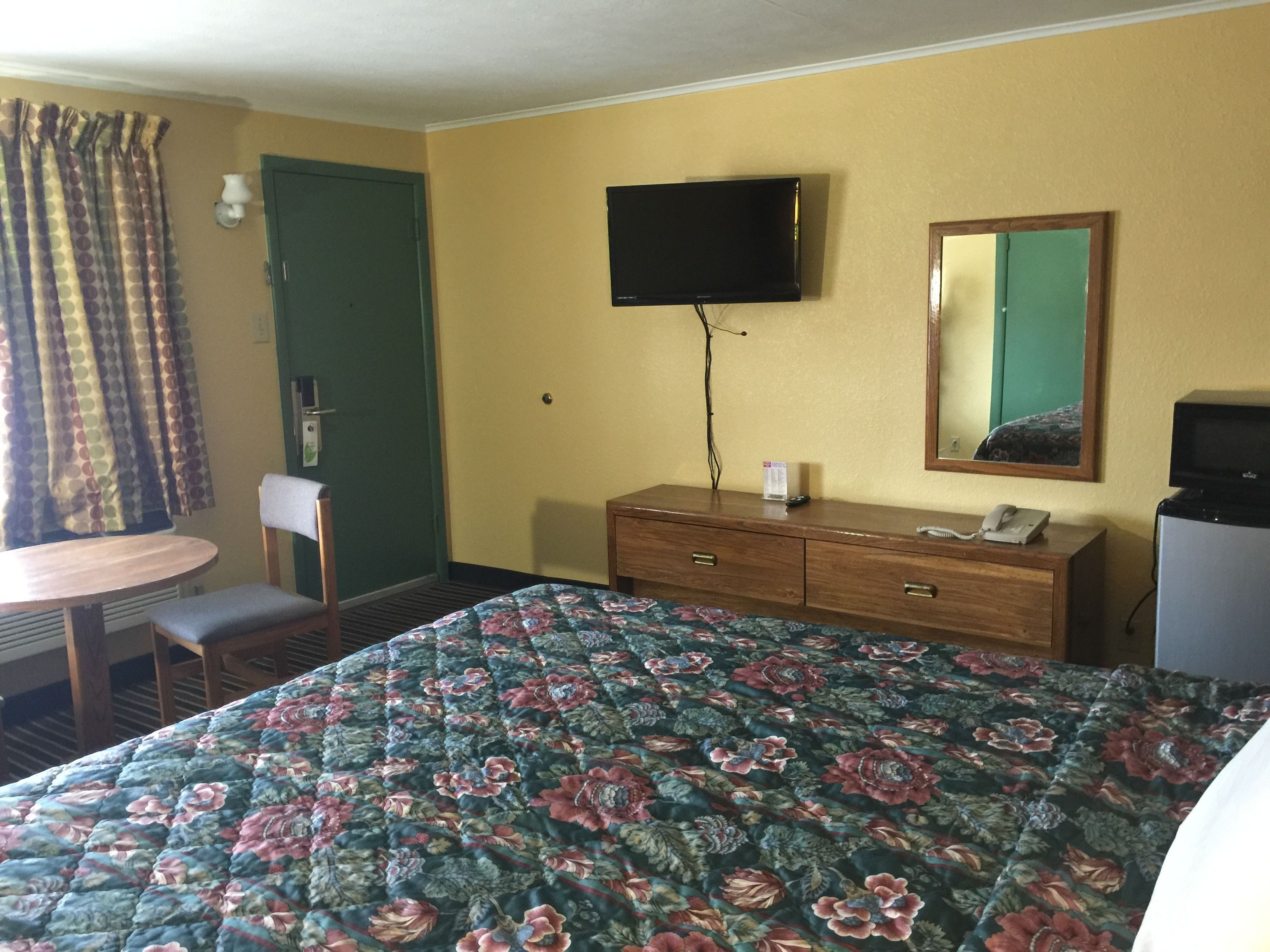 A hotel room with a bed, a desk, a chair, a dresser, a television, and a mirror.