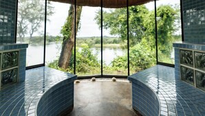 Una habitación con un banco azul de azulejos curvos, ventanas amplias con vistas a un lago y árboles, y suelo de hormigón.