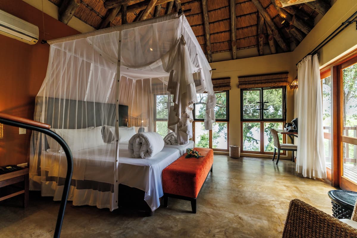 A room with a bed under a canopy, a bench, a table, and a chair.
