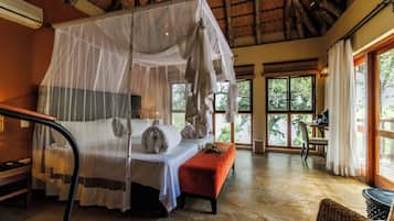 A room with a bed under a canopy, a bench, a table, and a chair.