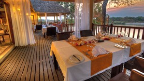Un restaurante con terraza de madera, manteles blancos y vistas al atardecer.