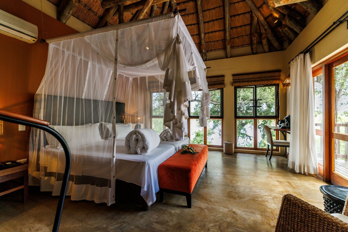 A room with a bed under a canopy, a bench, a chair, and a piano.