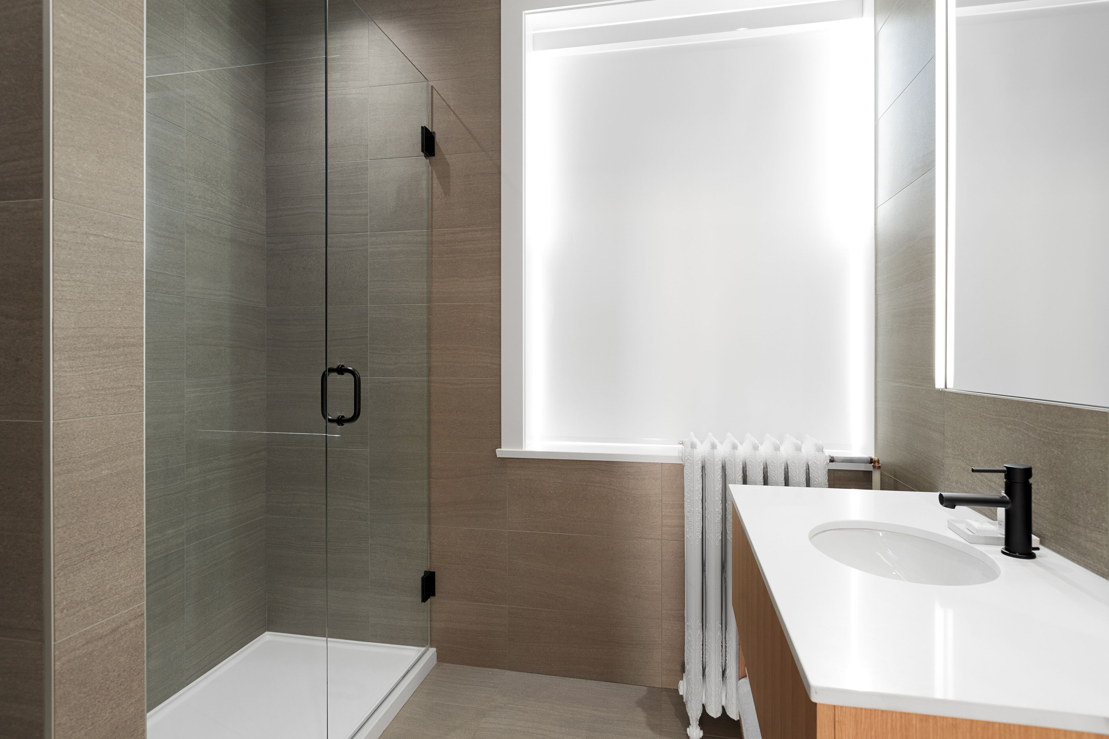 Een moderne badkamer met een douchecabine van glas, een witte wastafel en een grote spiegel.