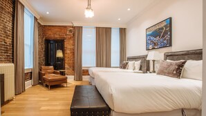 A hotel room with a brick wall, a fireplace, a large bed, a bench, and a painting on the wall. - Victorian Hotel (Vancouver)