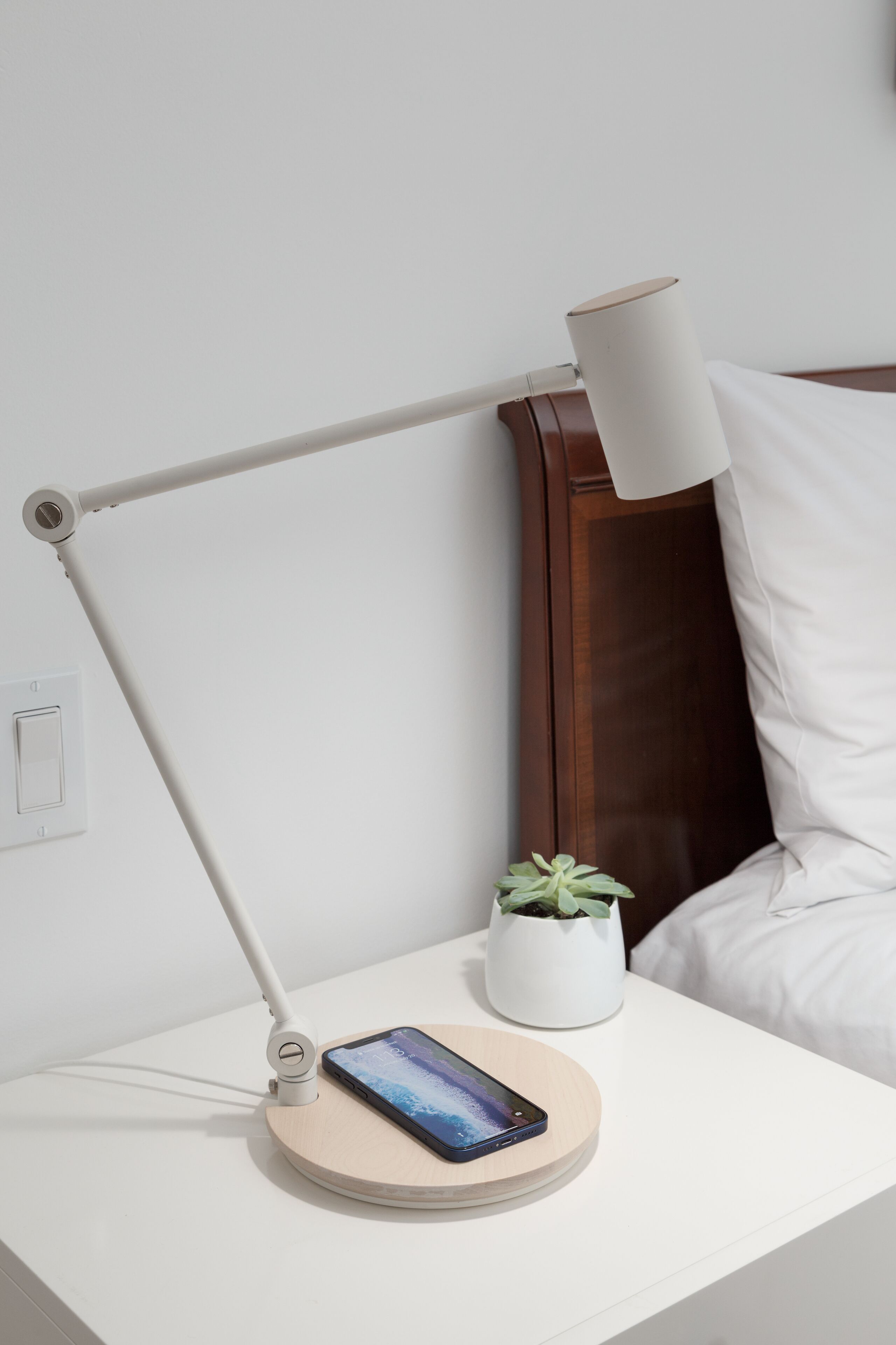 Een nachtkastje met een smartphone, een lamp en een kleine plant in een pot.