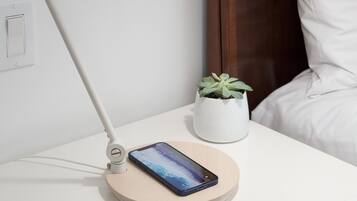 Een nachtkastje met een smartphone, een lamp en een kleine plant in een pot.