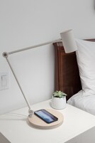 Una mesita de noche con un teléfono inteligente, una lámpara y una pequeña planta en maceta.
