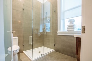 A modern bathroom with a glass-enclosed shower, a toilet, and a window with towels.