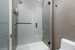 A modern bathroom with a glass-enclosed shower, a white toilet, and a tiled wall. - Victorian Hotel (Vancouver)