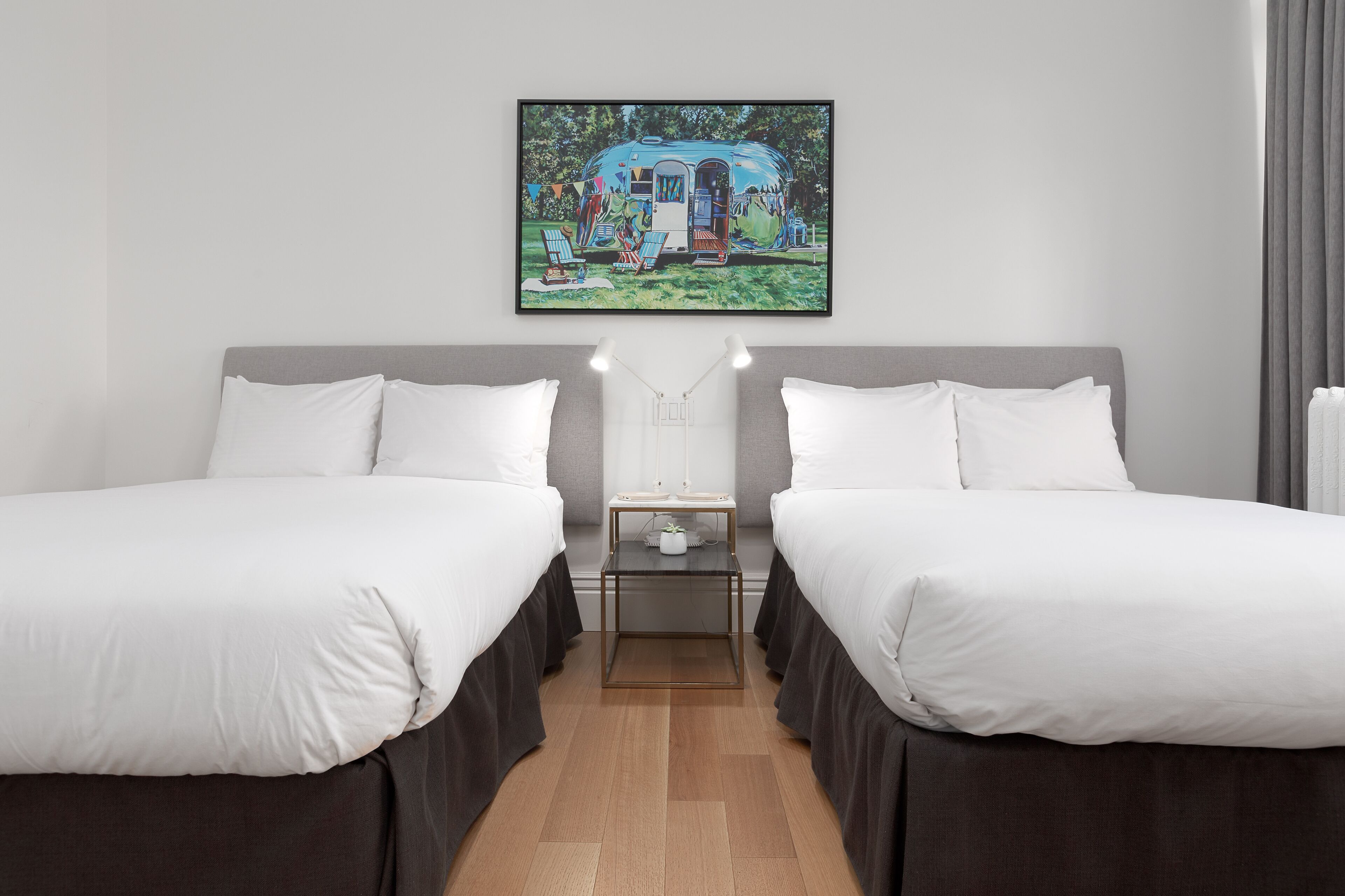 Habitación de hotel con dos camas, una mesita y un cuadro de una autocaravana.