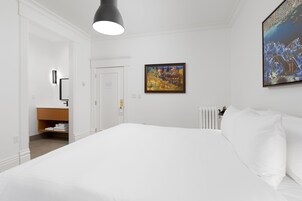 Una habitación de hotel con una cama grande, un cuadro en la pared y un baño visible a través de una puerta abierta.