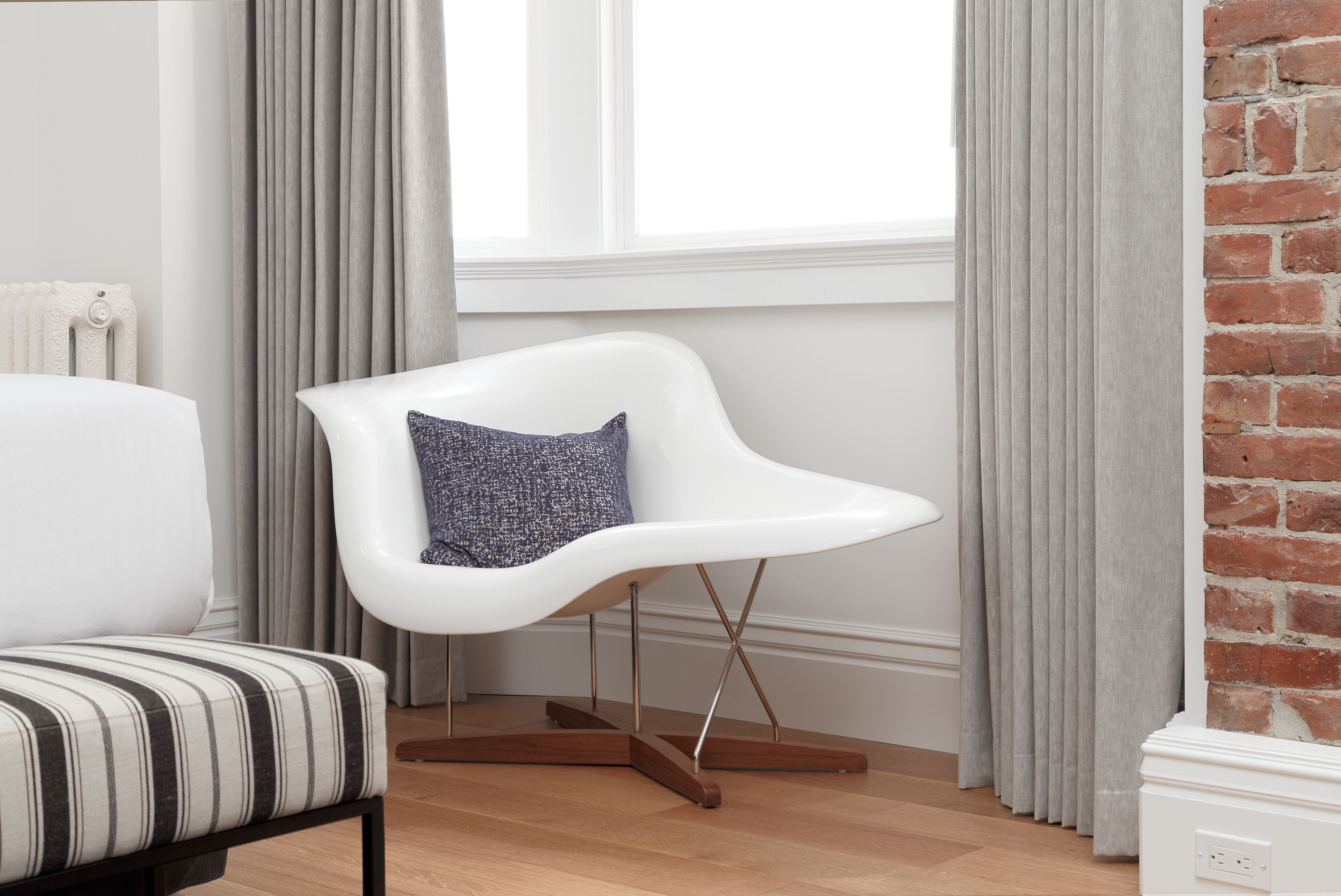 A modern living room with a white armchair, a striped sofa, and a patterned pillow.