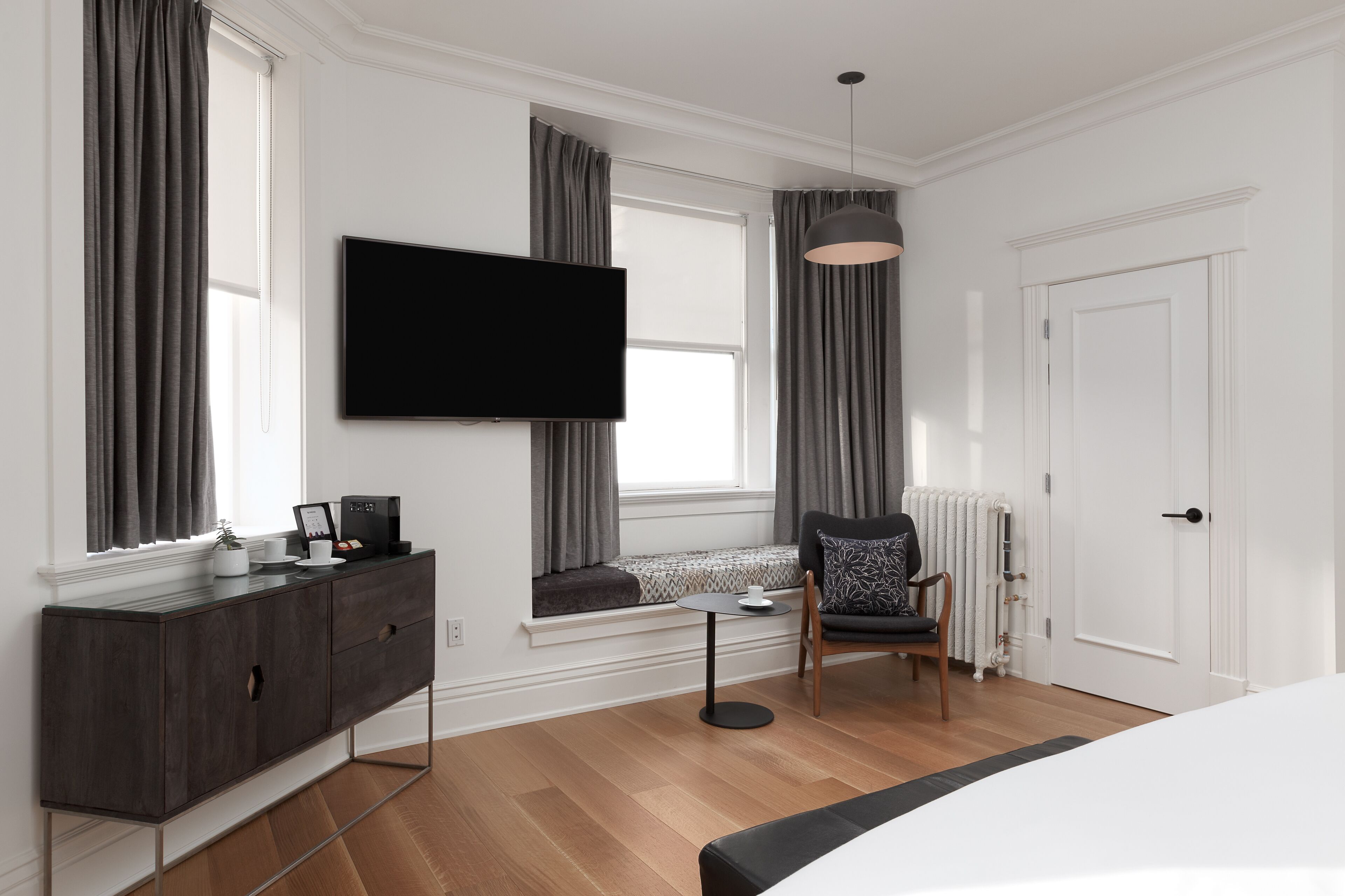 Een moderne hotelkamer met een grote flatscreen televisie, een donker houten kast, een klein rond tafeltje, een comfortabele stoel en een groot bed.