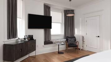 Een moderne hotelkamer met een grote flatscreen televisie, een donker houten kast, een klein rond tafeltje, een comfortabele stoel en een groot bed.
