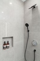 Um chuveiro moderno com um chuveiro de mão e comando na parede. Há duas garrafas de shampoo em uma prateleira pequena.
