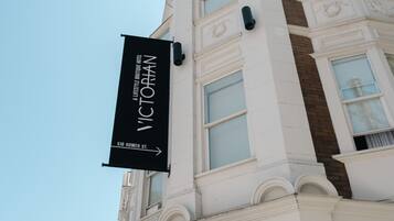 A building with a black banner reading 'A LIFESTYLE BOUTIQUE THE VICTORIAN' and a storefront with a black awning labeled 'Locanda del Vino.'