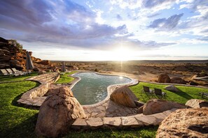 A landscaped pool area with stone pathways, large rocks, and lounge chairs.