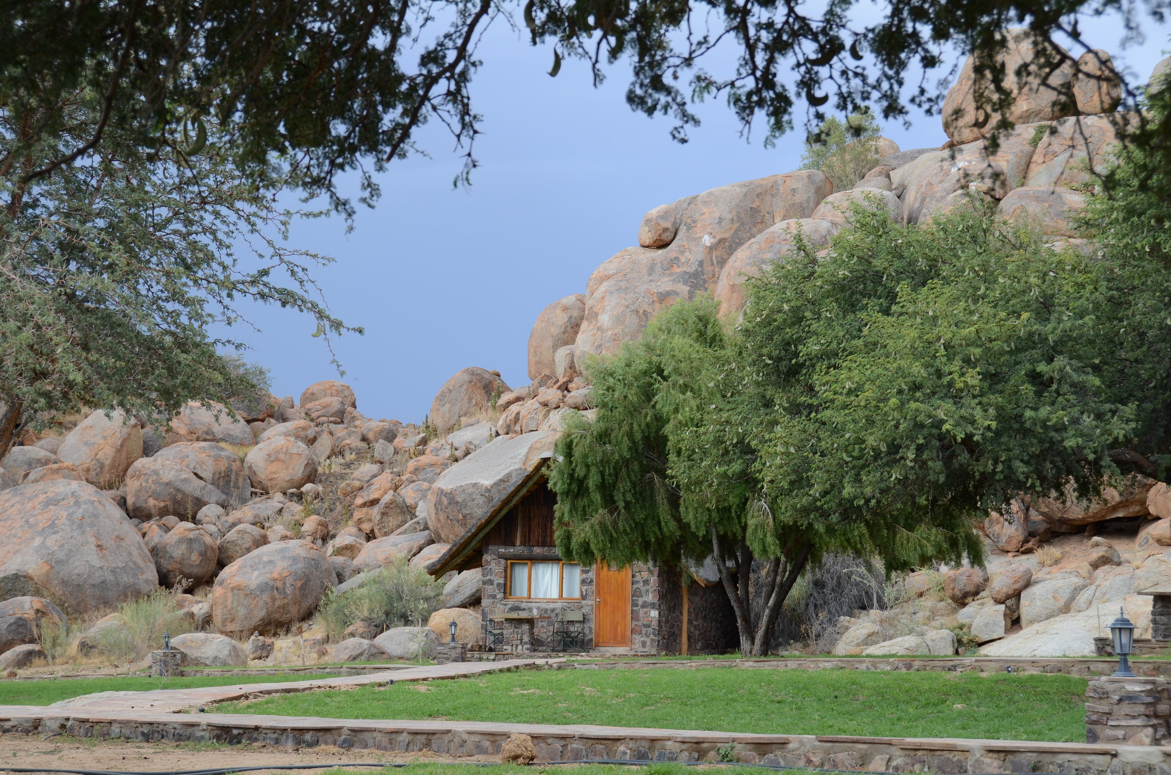 A rustic cabin with a stone exterior, surrounded by large boulders and a tree.