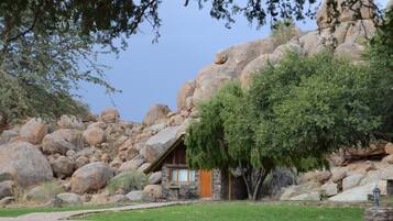 A rustic cabin with a stone exterior, surrounded by large boulders and a tree.