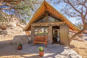 Una cabaña de piedra con techo de madera, un banco y dos macetas con plantas.