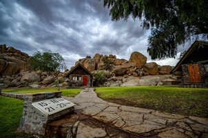 Un edificio de piedra rústica con una puerta roja, rodeado de rocas grandes y un sendero de piedra.
