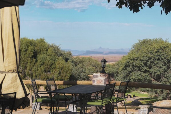 An outdoor dining area with a table and chairs, a lamp, and a view of a mountainous landscape.