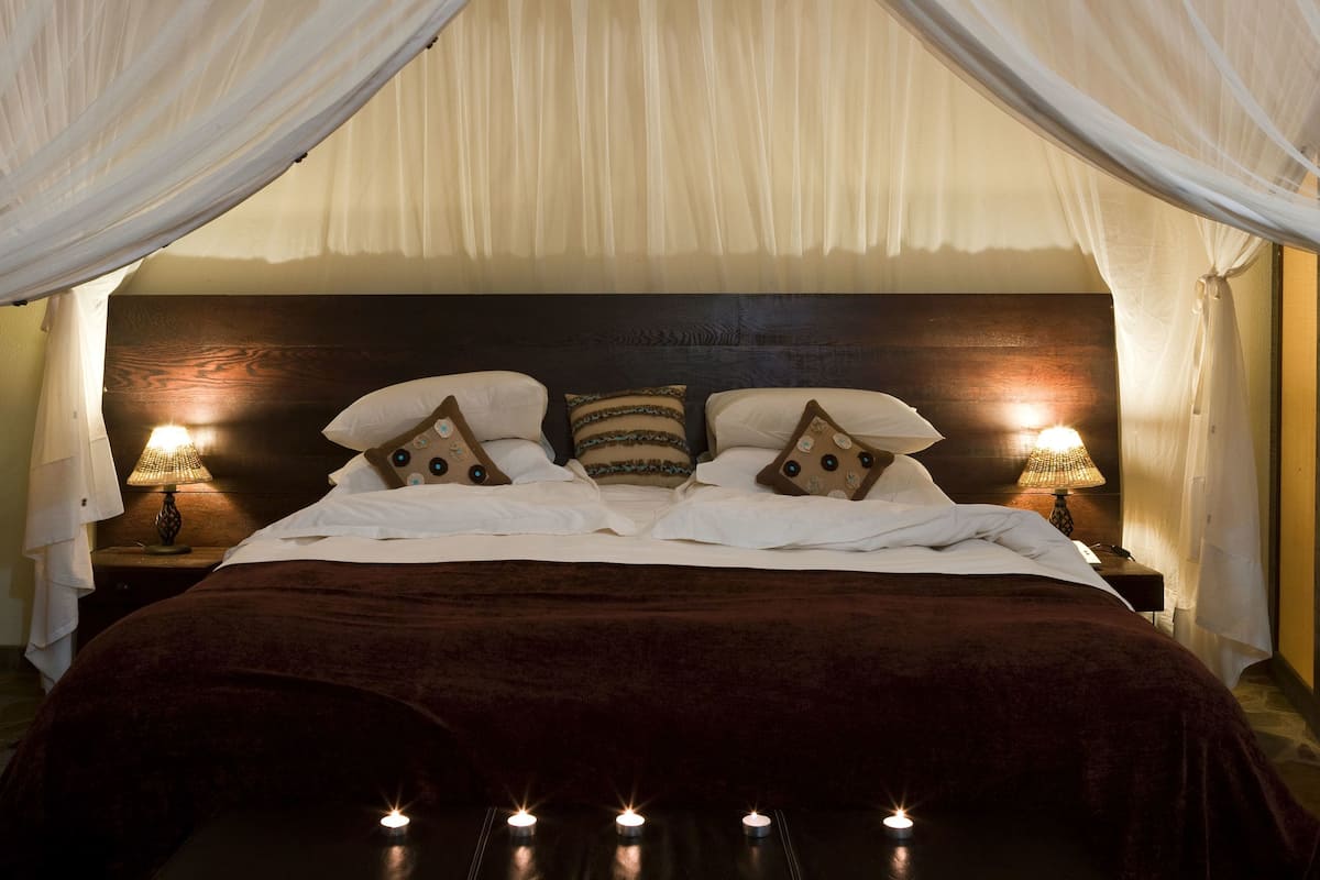 A bed with white bedding, multiple pillows, and a dark headboard. There are two bedside lamps and candles on the floor.