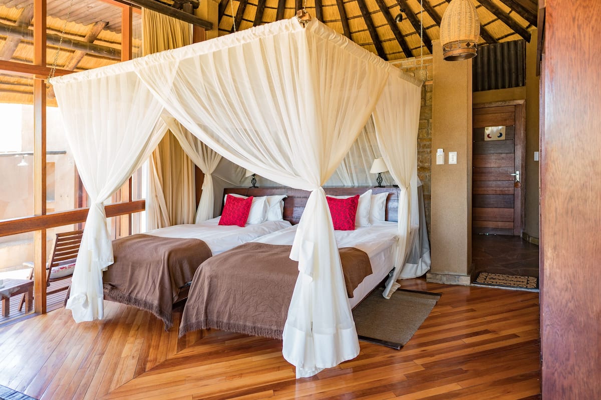 A room with a wooden floor, a bed with a canopy, and a staircase.