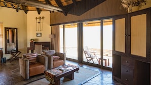 A spacious living area with a high ceiling, large windows, and a view of the outdoors. There are leather sofas, a coffee table, and a wooden cabinet.
