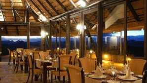 An outdoor dining area with tables set for two, featuring wicker chairs and a view of the mountains.