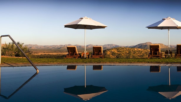 A pool with clear water reflecting the surrounding landscape, wooden lounge chairs, and umbrellas.